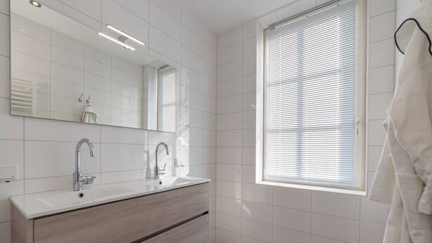 A modern bathroom with a large mirror, two sinks, a vanity, and a window with blinds. - Luxury stay with sauna, spa-bath near the beach (Colijnsplaat)