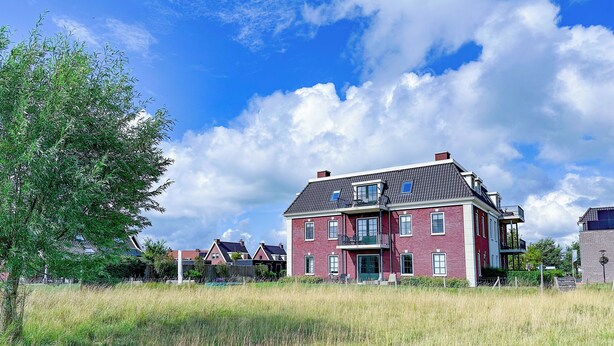 A large two-story house with a balcony and a fenced yard. - Luxury stay with sauna, spa-bath near the beach (Colijnsplaat)
