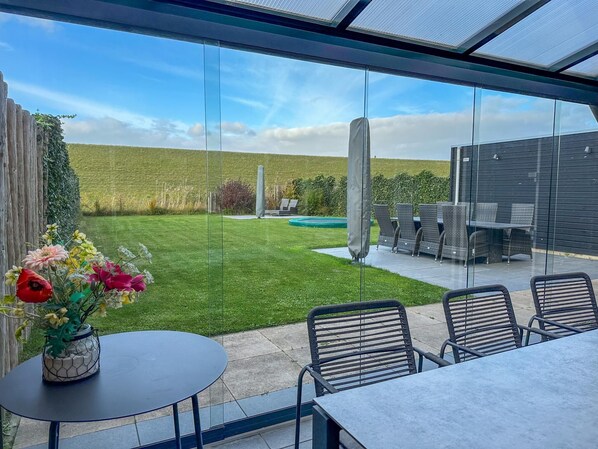 A patio area with a table and chairs, a flower arrangement, and a view of a grassy field and a building in the background.