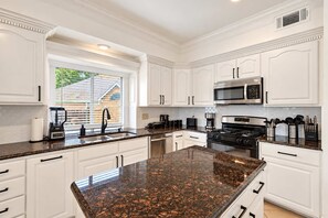 A modern kitchen with white cabinetry, granite countertops, a stainless steel stove, and a window with blinds.