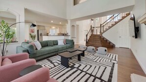 A spacious living area with a green sofa, a coffee table, and a patterned rug. A staircase leads to an upper level.