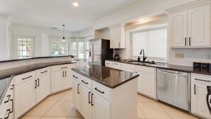 A spacious kitchen with white cabinetry, a granite countertop, stainless steel appliances, and a large window with blinds.