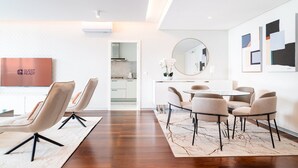 A modern hotel room with a dining area, a TV displaying "GUEST READY", and a kitchen visible through an open door.