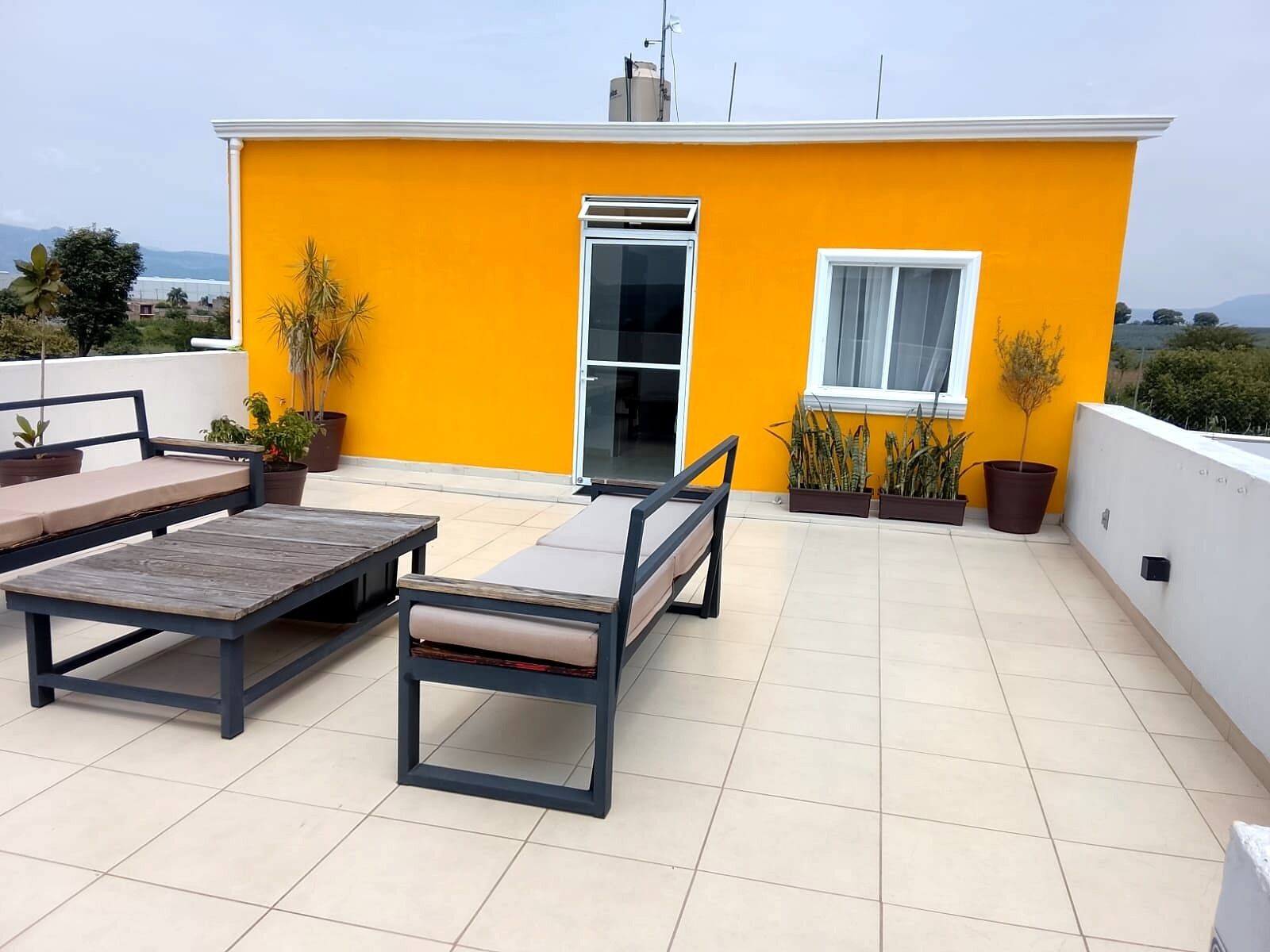 A rooftop terrace with a yellow wall, a sliding glass door, and a seating area with a table and chairs.