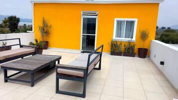 A rooftop terrace with a yellow wall, a sliding glass door, and a seating area with a table and chairs.