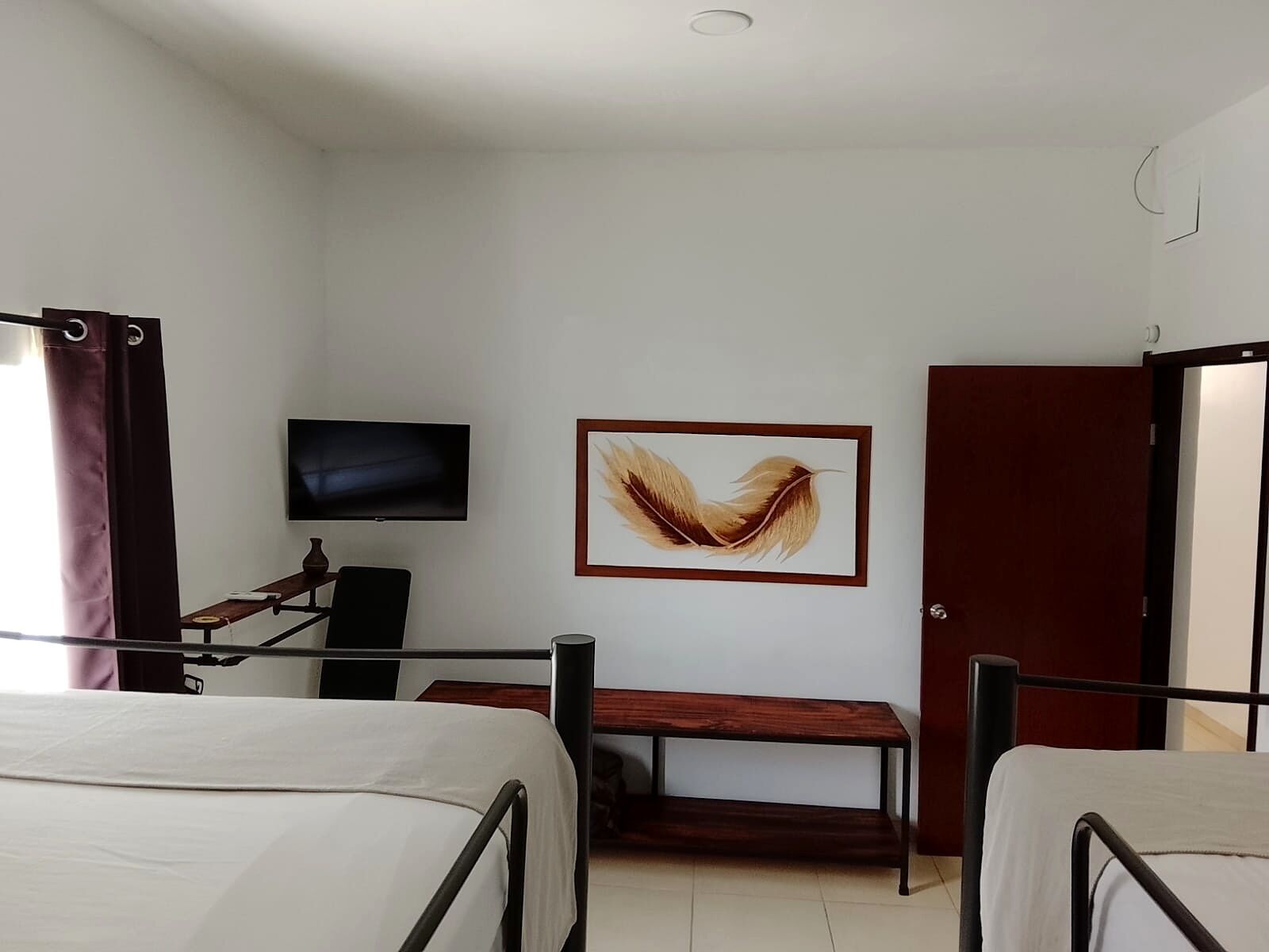 Een hotelkamer met twee bedden, een televisie, een lijst met een kunstwerk en een deur.