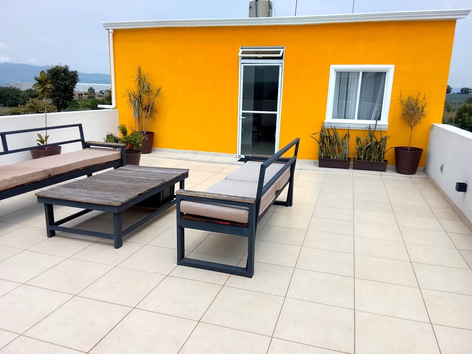 A rooftop terrace with a yellow wall, a sliding glass door, and outdoor furniture including a table and two chairs.