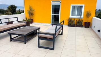 A rooftop terrace with a yellow wall, a sliding glass door, and outdoor furniture including a table and two chairs.