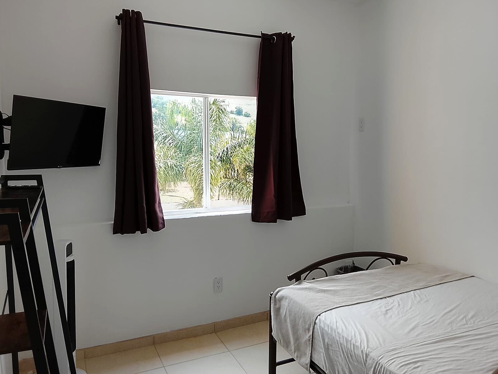 A room with a bed, a television mounted on the wall, and a window with curtains.