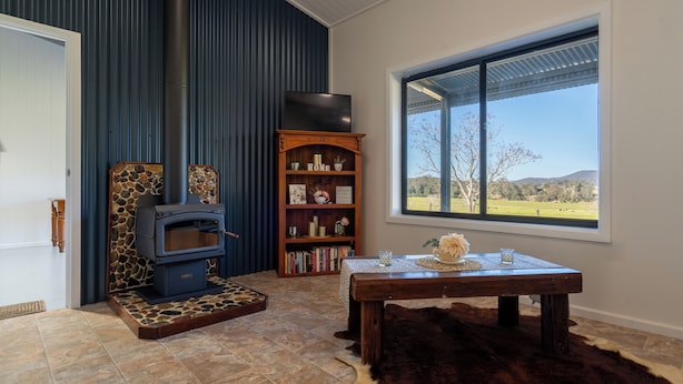 A cozy room with a stone fireplace, a bookshelf, and a large window offering a view of the outdoors.