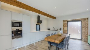 A modern kitchen with built-in appliances, a dining area with a wooden table and chairs, and a large window with a view. - 3 bedroom accommodation in East Firsby (East Firsby)