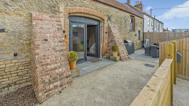 A stone building with a tiled roof, a wooden fence, and a gravel patio. - 3 bedroom accommodation in East Firsby (East Firsby)