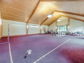 Un terrain de badminton intérieur doté d’un sol violet, d’un plafond en bois et éclairé par la lumière naturelle qui entre par de grandes fenêtres.