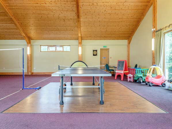 Una mesa de ping pong en una habitación con vigas de madera, un dardo y juguetes infantiles.