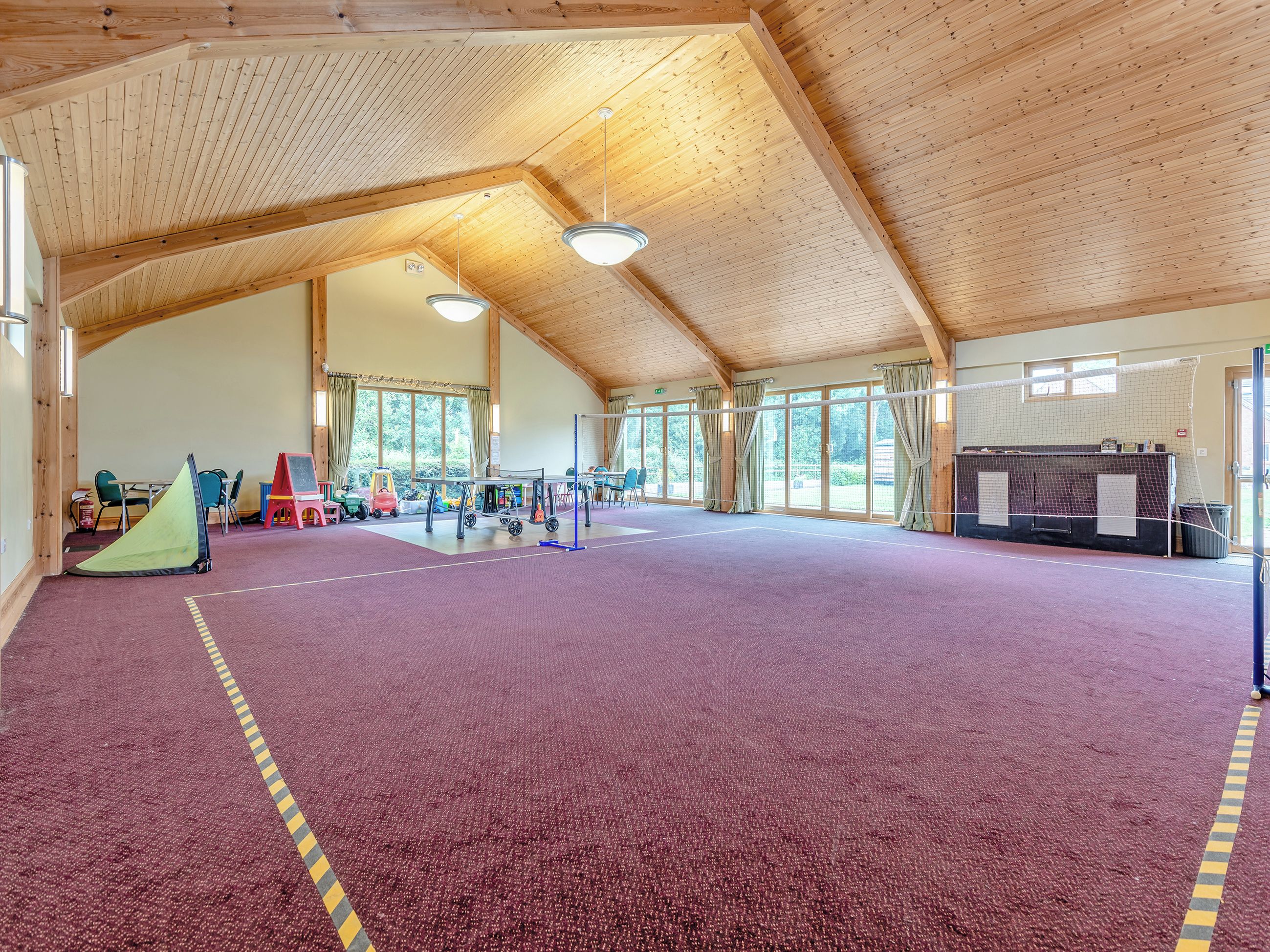 A spacious indoor area with a high wooden ceiling, a purple carpeted floor, and various sports equipment.