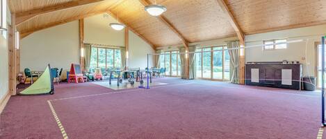 A spacious indoor area with a high wooden ceiling, a purple carpeted floor, and various sports equipment.