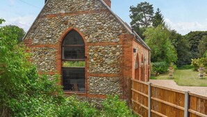 A stone building with a triangular roof, a large arched window, and a wooden fence in front.