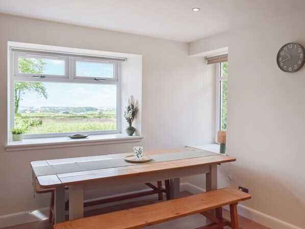 A room with a wooden table, bench, and a window with a view of greenery.