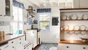 A kitchen with white cabinets, a stove, and a window. There are pots hanging on the wall, and a chalkboard with notes. - 3 bedroom accommodation in Aberystwyth (Aberystwyth)