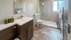 A modern bathroom with a wooden vanity, a white sink, a shower area, and a chair.