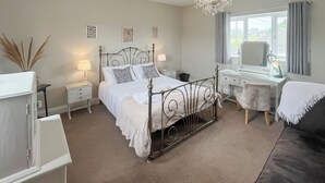 A bedroom with a four-poster bed, a desk with a chair, a vanity with a mirror, and a chandelier.
