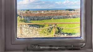 A window with a view of a stone wall, grassy field, and distant hills. - Ty'r Bugail Shepherds Hut (Tal Y Bont, near Barmouth)