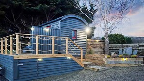 A small, single-story wooden cabin with a deck and a staircase leading to a door. - Ty'r Bugail Shepherds Hut (Tal Y Bont, near Barmouth)