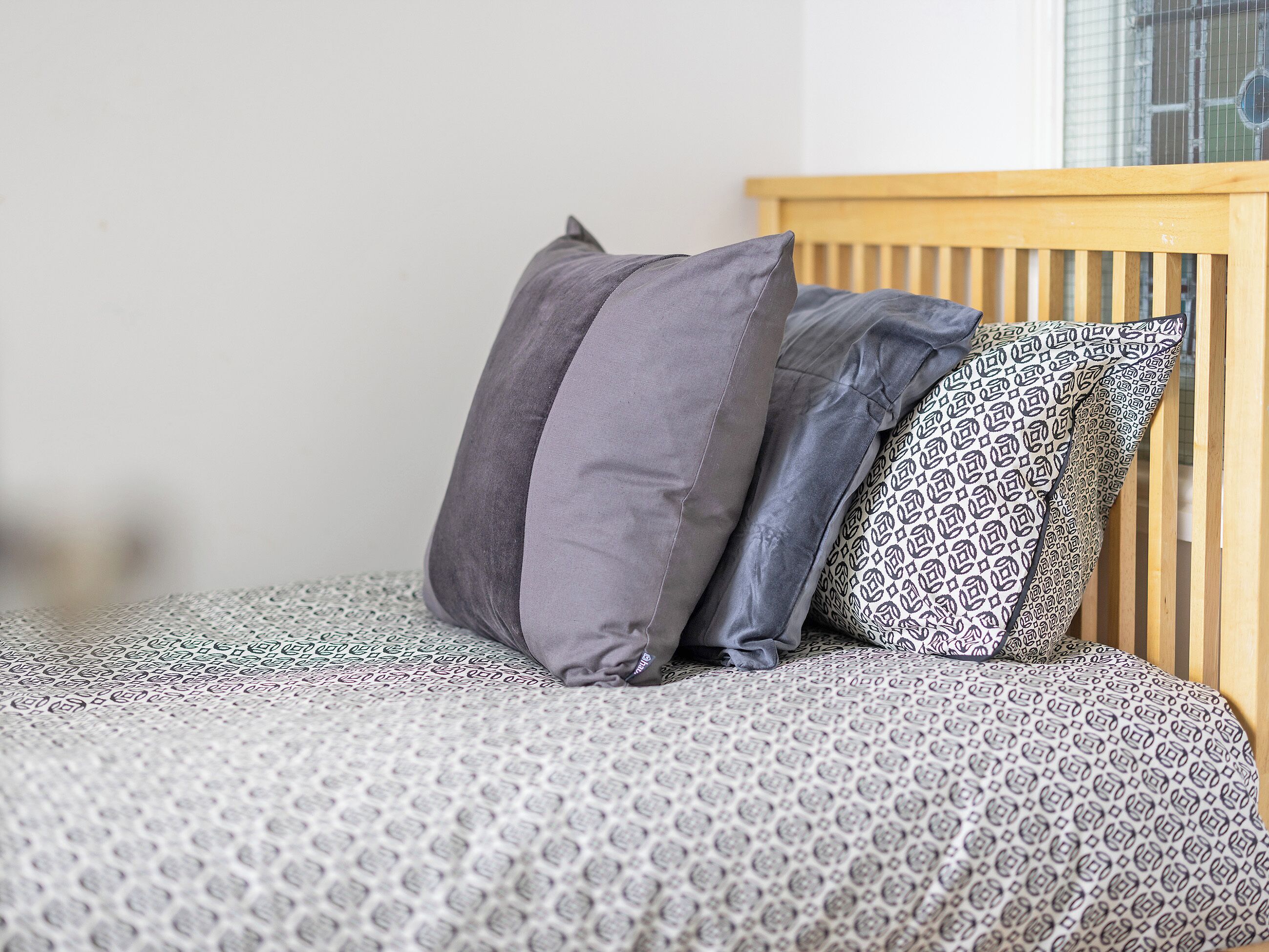 A bed with patterned bedding and two pillows, one plain and one with a geometric design.