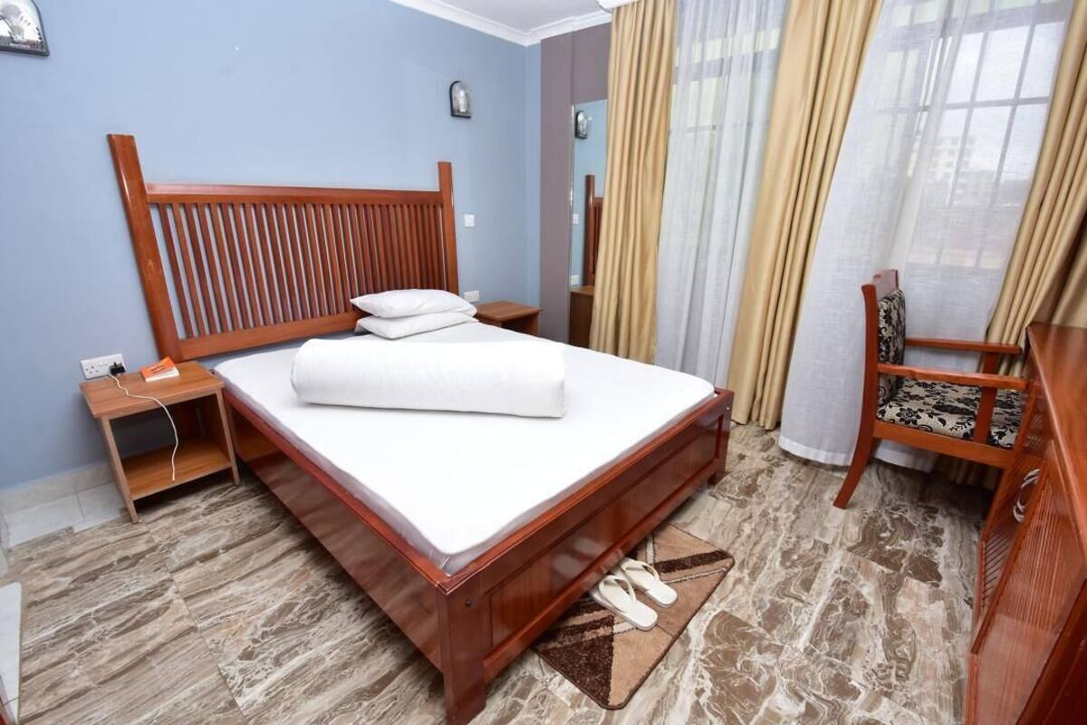 Une chambre d’hôtel avec un lit en bois, une table de chevet, une chaise et une armoire.