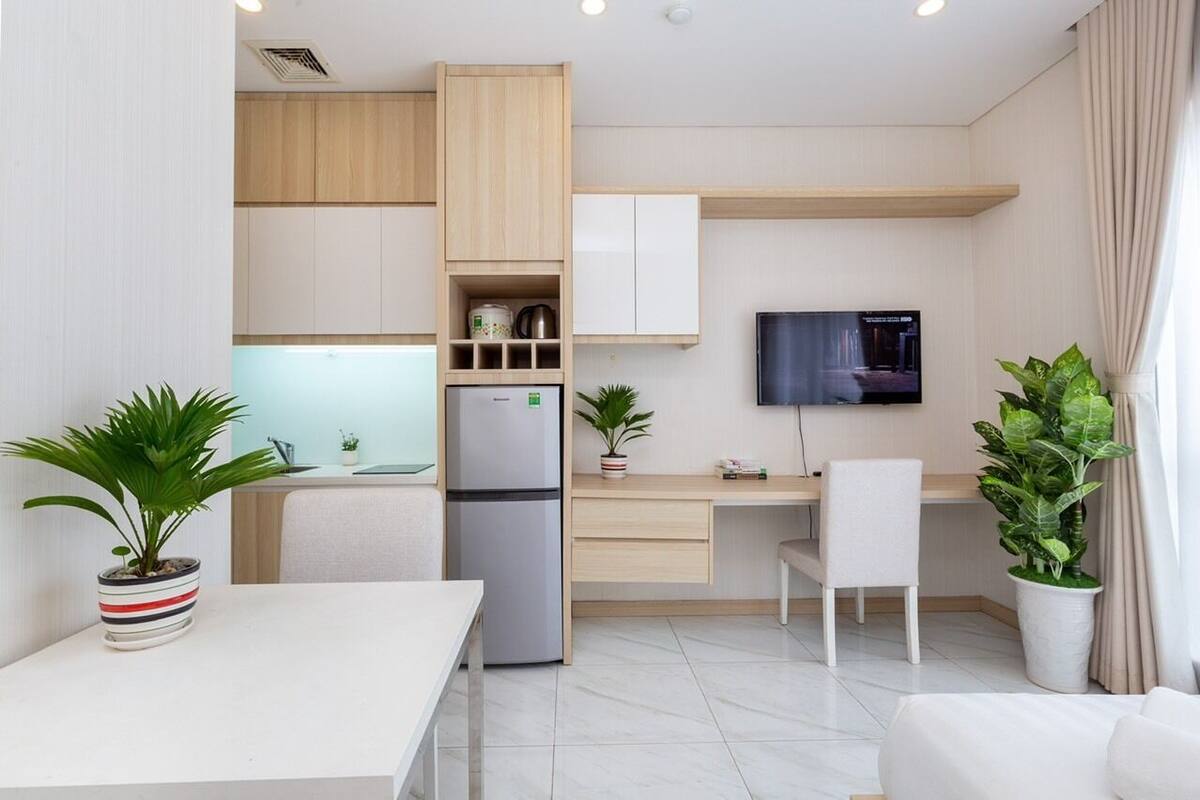 Una cocina moderna con un refrigerador empotrado, un mueble de madera y un televisor montado en la pared. Hay dos plantas en macetas y una mesa de comedor con sillas.