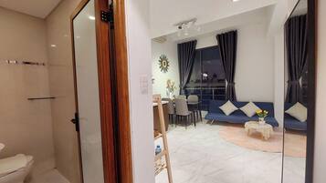 A modern living room with a sofa, a dining table, and chairs. There is a bathroom with a toilet visible.