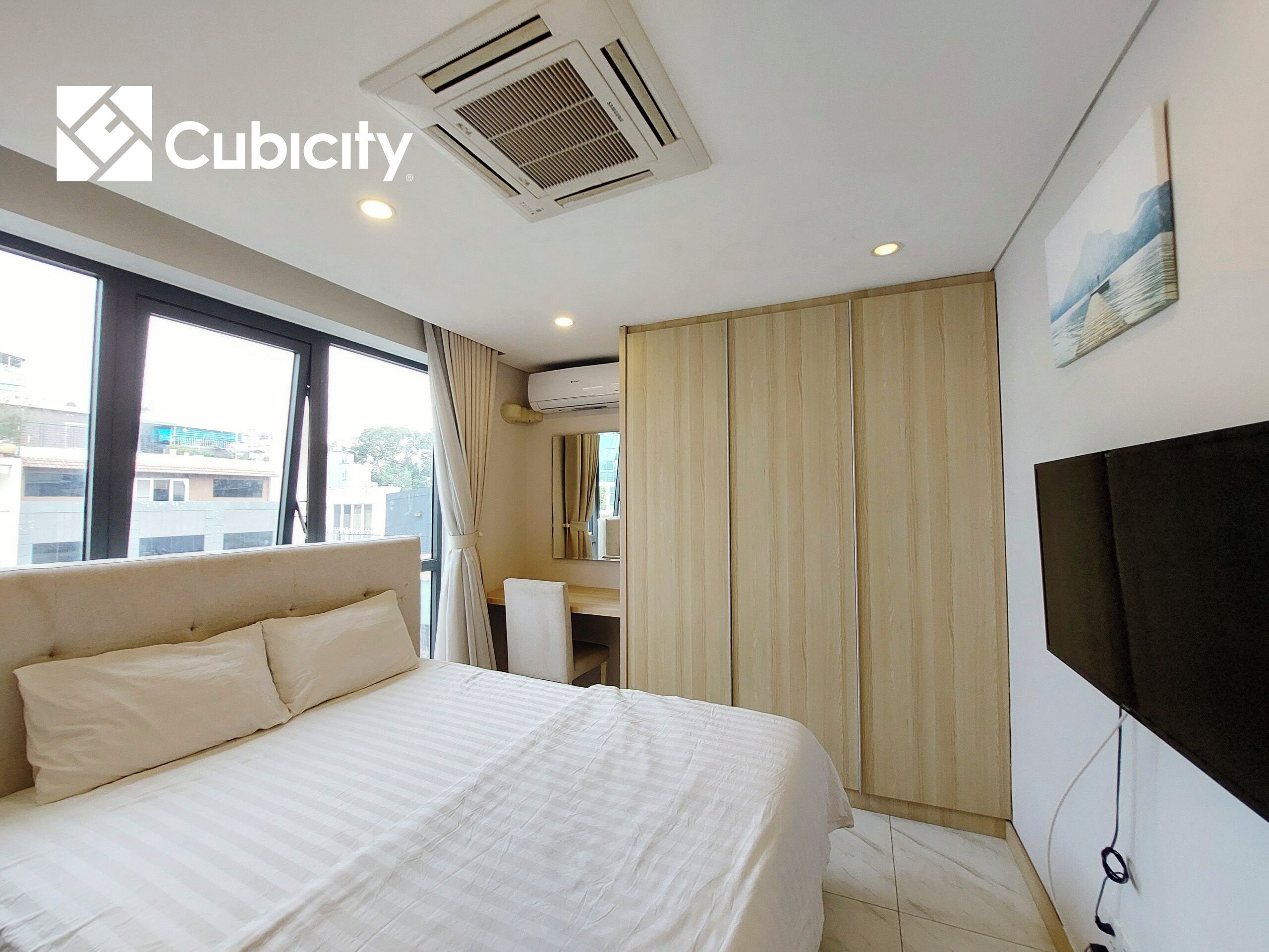 Habitación de hotel con cama, escritorio, silla, equipo de aire acondicionado, televisión y ventana con cortinas.