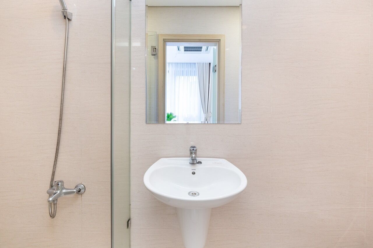 Une salle de bain avec un lavabo blanc, une douchette à main et un miroir au-dessus du lavabo.