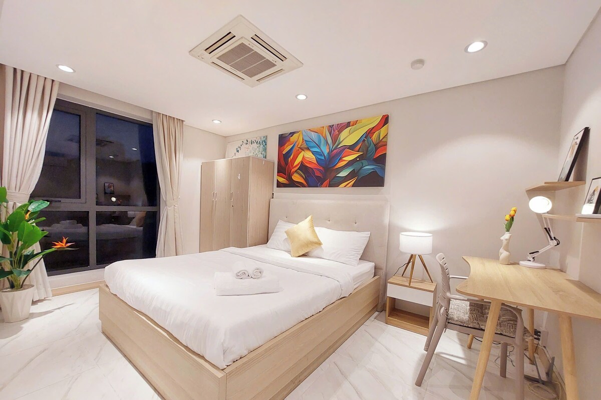 A modern bedroom with a bed, bedside table, desk, and a large window.