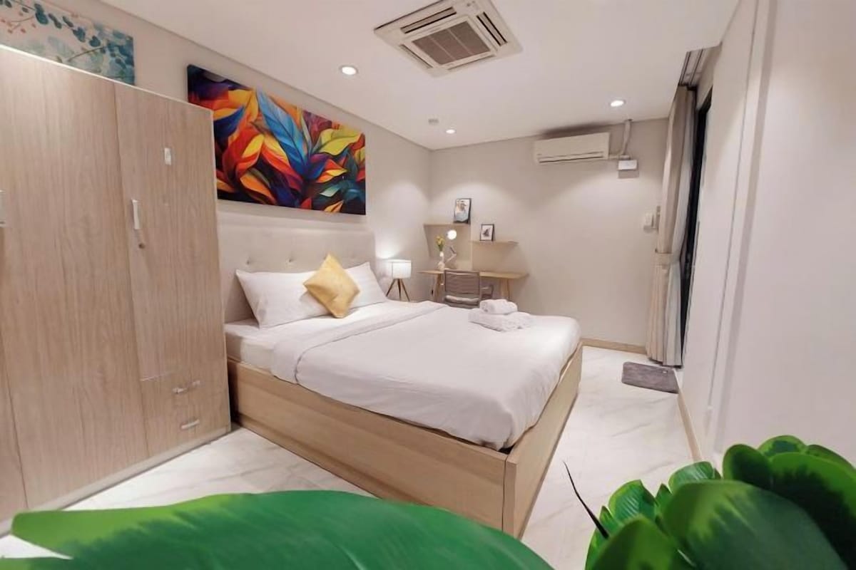 Un dormitorio moderno con cama, armario, mesita de noche, lámpara y un cuadro abstracto y colorido en la pared.