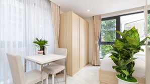 A modern room with a dining table, chairs, a large potted plant, and a window with curtains. - Cubicity Hidden House (Ho Chi Minh City)