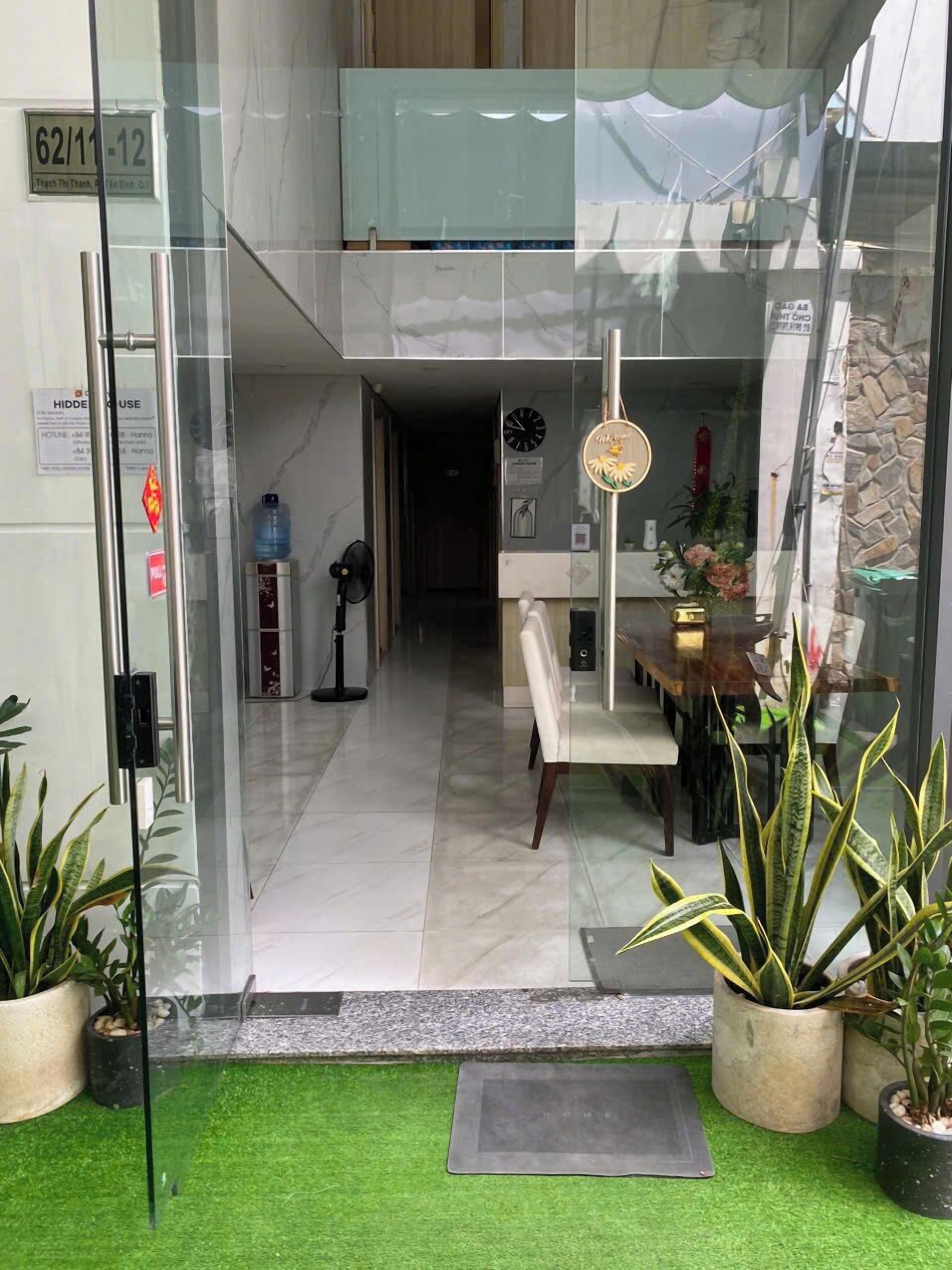 A hotel entrance with a glass door, a reception desk, a clock, and a sign indicating a hidden room.