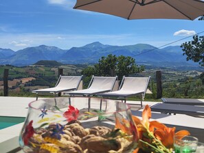 A terrace with lounge chairs and a table with a floral arrangement, overlooking a mountainous landscape. - GrazieSole Farmhouse—entire house for exclusive use, with a view of the Sibillini Mountains (Penna San Giovanni)