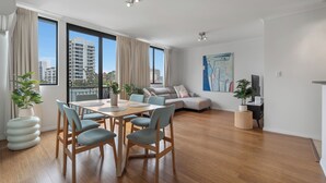 A modern living room with a dining area, large windows, and a city view. - Central Urban Nest with Pool (Perth)