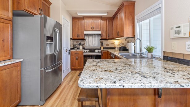 Una cocina con armarios de madera, electrodomésticos de acero inoxidable, encimera de granito y una ventana con persianas.