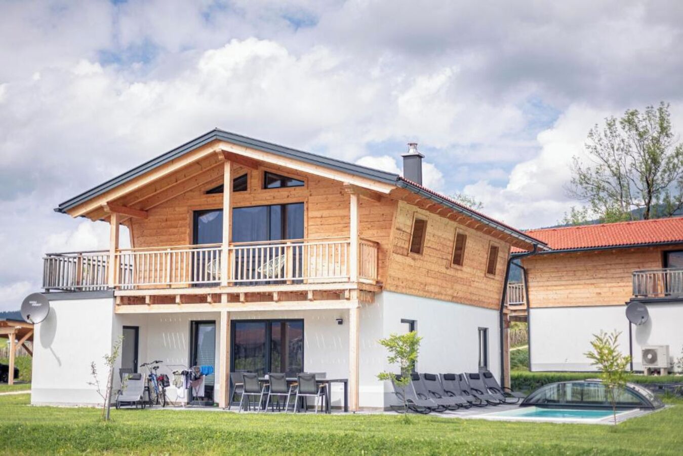 A two-story wooden house with a balcony, a swimming pool, and outdoor seating.