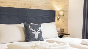 Una cama bien hecha con sábanas blancas, cabecera oscura y almohada con diseño de cabeza de ciervo.