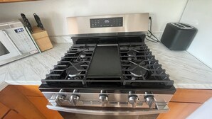 Ein Herd aus Edelstahl mit digitaler Bedieneinheit, eine Mikrowelle und ein Toaster auf einer Marmorarbeitsplatte.