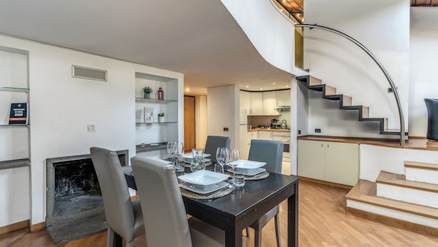 Un espace de repas moderne avec une table noire dressée pour quatre personnes, une cheminée et un escalier en colimaçon menant à un niveau supérieur.