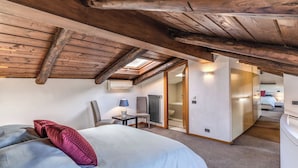 Une chambre avec un puits de lumière, un lit avec des oreillers, un bureau avec une lampe et une vue sur une autre pièce.