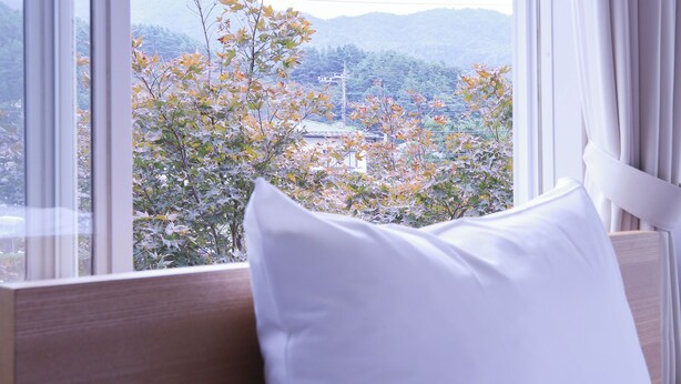 Una habitación de hotel con cama, ventana con cortinas y vistas a árboles y edificios.