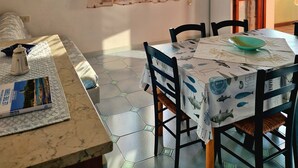 A dining area with a table set for two, a book on the table, and a view of the outside through a window with curtains. - Within walking distance of the beautiful Vignola beach, with panoramic terrace. (Vignola Mare)