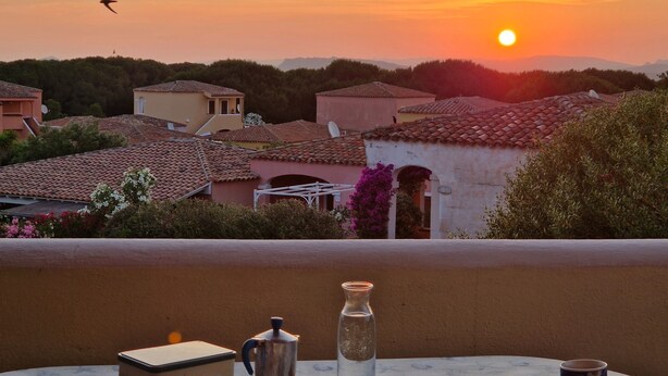 A terrace with a table set for breakfast, overlooking a village with traditional buildings and a sunset. - Within walking distance of the beautiful Vignola beach, with panoramic terrace. (Vignola Mare)