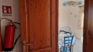 A wooden door leading to a room with a dining table, chairs, and a fire extinguisher mounted on the wall. - Within walking distance of the beautiful Vignola beach, with panoramic terrace. (Vignola Mare)