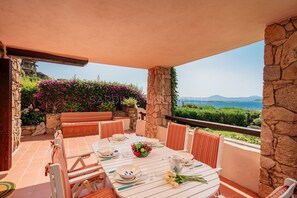 A dining area with a table set for four, surrounded by stone walls and a view of the sea.